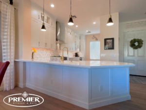 Contemporary kitchen remodel with white cabinets, a large island, pendant lighting, and decorative backsplash by Premier Kitchen & Bath