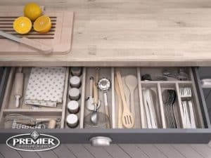 Drawer with organized pull-out cutlery cubbies, wooden utensils, and spices, featuring a cutting board with sliced oranges on the countertop